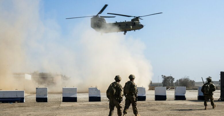 American troops walk as a US Army C-47 Chinook helicopter flies over the village of Oreij, south of Mosul, Iraq