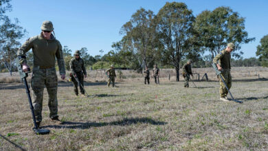 Seven uniformed personnel from the Australian Defence Force use metal detectors to search for potentially dangerous war remnants in a field in Nauru. They are deployed as members of the ordnance mission Operation Render Safe.