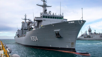 HMAS Stalwart, a Royal Australian Navy ship, is seen docked in a pier. It faces to the right, and "A304" is seen painted on its right side. On the middle right side of the background, another ship can be seen docked in the pier.