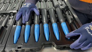 Six of Australia's Boxer Combat Reconnaissance Vehicle (CRV) ammunition are seen lined up in a tray in what appears to be a production line or factory. A worker carefully lines them up.