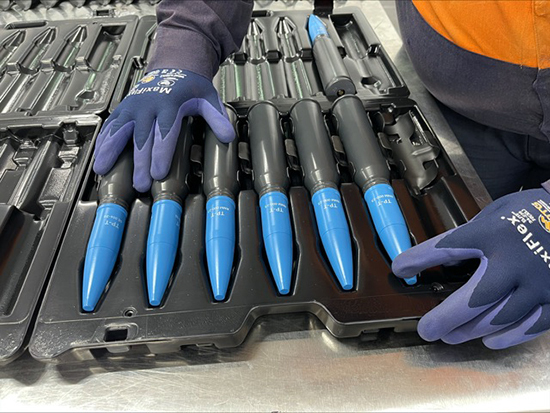 Six of Australia's Boxer Combat Reconnaissance Vehicle (CRV) ammunition are seen lined up in a tray in what appears to be a production line or factory. A worker carefully lines them up.