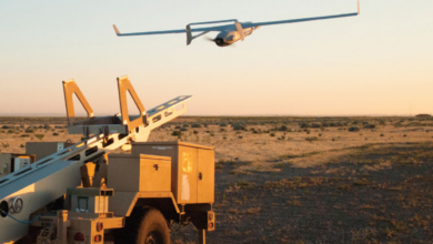 An Insitu Integrator drone is seen taking off, seemingly launched by a wheeled launcher on the left side of the image. The sunset tinges the whole scenery with a bright, warm orange hue.