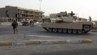An M1A1 Abrams tank provides area security alongside a street intersection beside Marines during a 2005 operation in Fallujah, Iraq