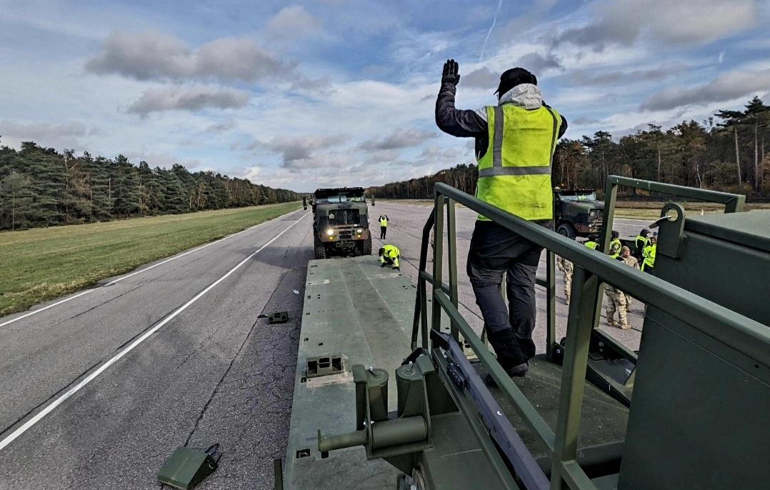 A Belgian host nation employee from Army Field Support Battalion-Benelux, 405th Army Field Support Brigade, ground guides an M1300 Enhanced Heavy Equipment Transporter onto an M1302 trailer at the Zutendaal Army Prepositioned Stocks-2 worksite in Belgium during an EHET drivers academy held there NOV. 6-22. (U.S. Army courtesy photo)