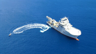 HMNZS Manawanui (A09) is seen sailing in the water as a smaller seacraft sails from it to the left. "A09" is painted in black on the right side of its grey hull.
