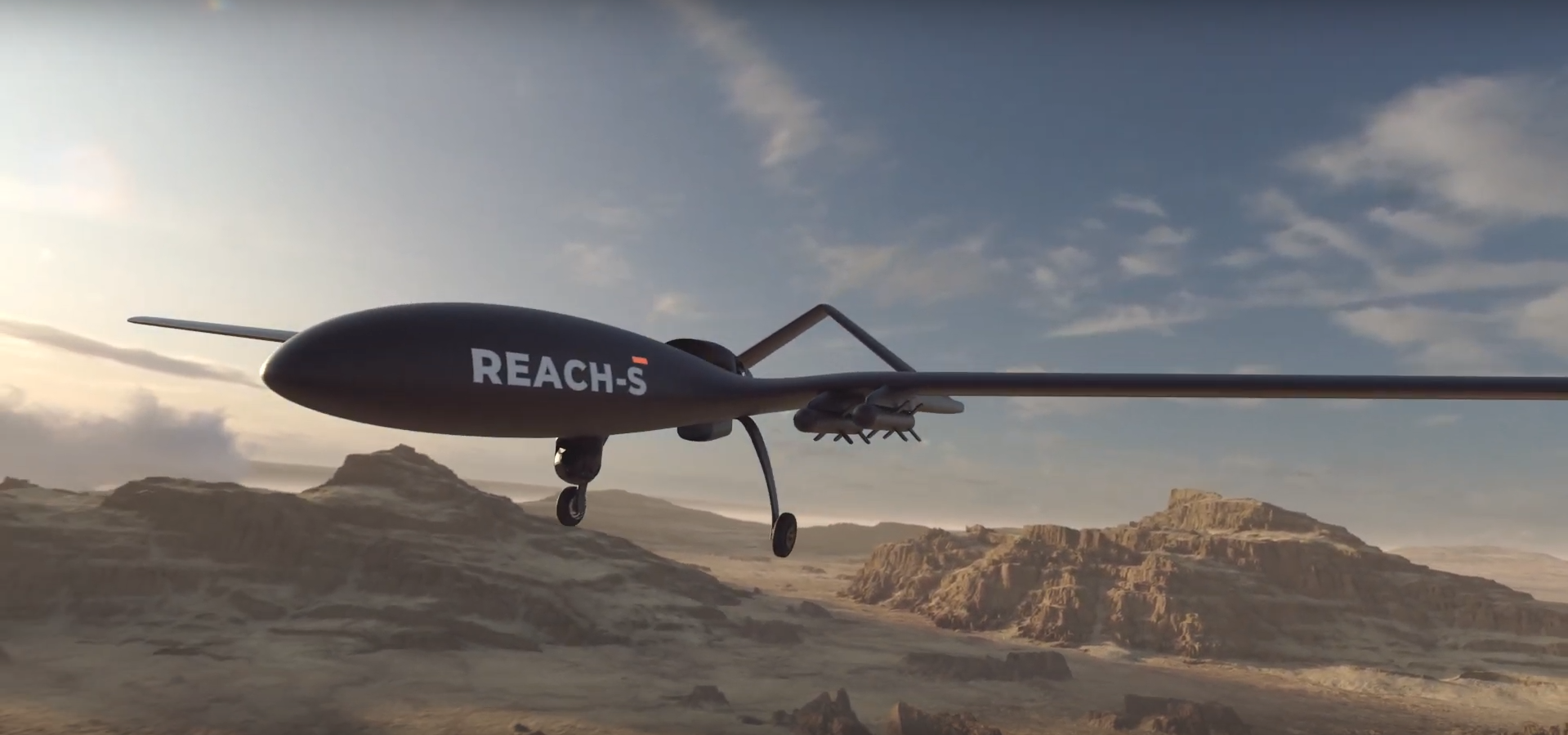 A 3D rendering of EDGE's REACH-S unmanned aerial vehicle (UAV) is seen flying over a dry, mountainous desert landscape. The sky is a dull blue with the sun casting light shadows as it begins to set offscreen.