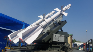 The Surface-to-Air Missile for Assured Retaliation (SAMAR) missile ssytem is seen in the middle of the frame. The launcher is painted a deep green. Two missiles, painted white, are propped on it, pointing upwards. The background is a light blue sky.
