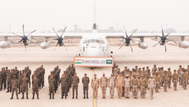 Uniformed soldiers from the Indian and Saudi Arabian Army stand in attention in front of a white plane in what appears to be an airport runway. Between the soldiers and the aircraft, a huge banner reads 'EX SADA TANSEEQ - 2024'. India's flag is on the leftmost side of the banner, while Saudi Arabia's is on the right. The background is a foggy gray sky with a barely visible skyline in the distance.