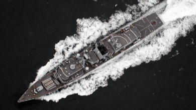 A UK Royal Navy ship is seen sailing deep dark-blue waters. The scene is shown from a top-down view.
