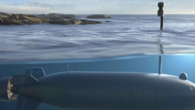 An artist's rendering of an uncrewed combat underwater vehicle. The drone is submerged underwater, while its periscope sticks out the water's surface. A rocky shore is seen over on the left side of the horizon.