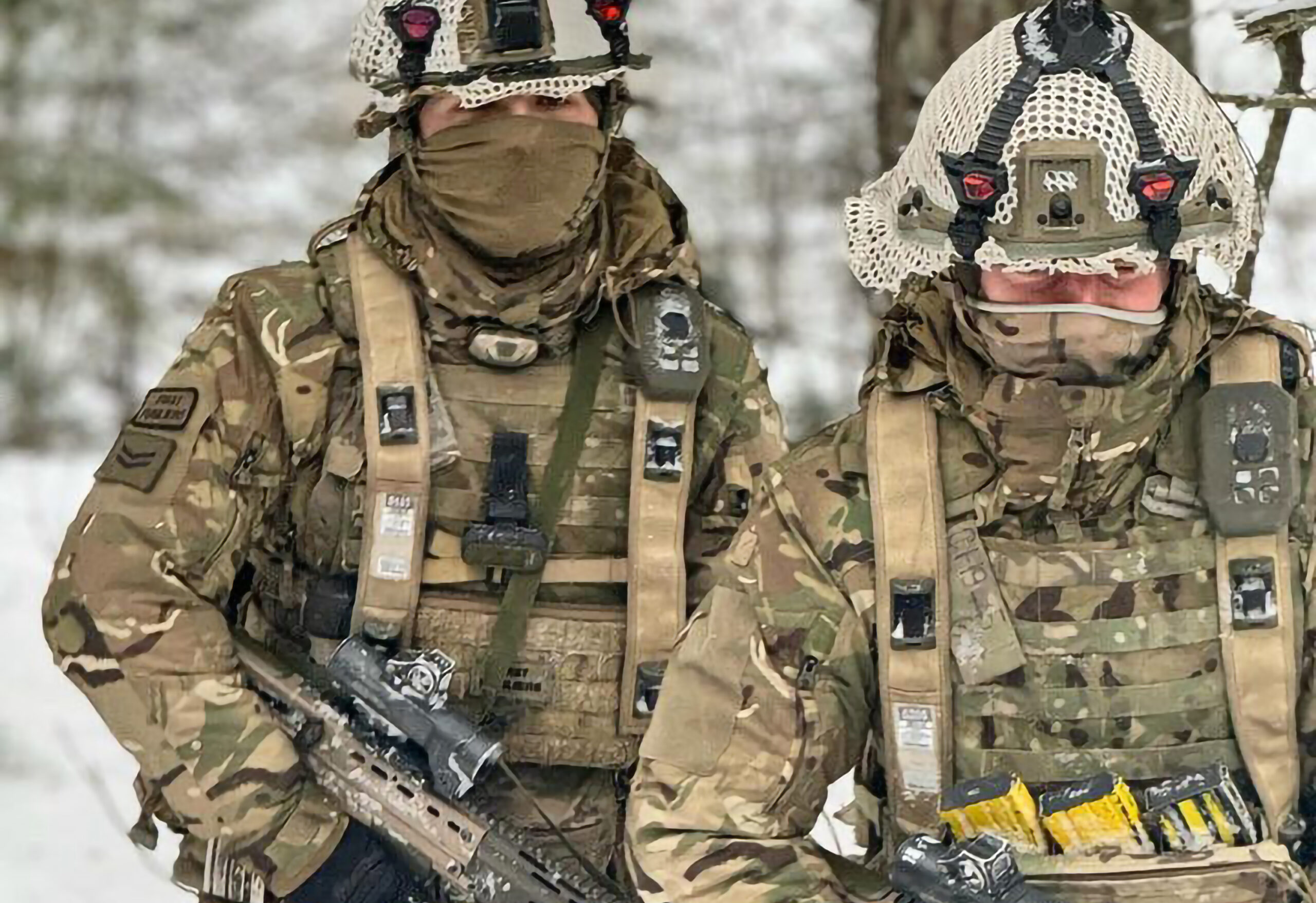 Two camouflaged soldiers appear to be wearing Saab's live training equipment, which tracks the soldiers during training with laser and geometric pairing technology. Various black straps and sensors can be seen attached to their helmets.