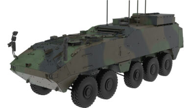 The Piranha Heavy Mission Carrier. The vehicle is painted in dark green, brown and black camouflage. It has ten wheels and is fitted with rigid armor. It has four antennae on its body all pointing upwards, and three sets of what appears to be side mirrors installed.