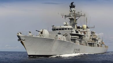 UK's HMS Lancaster warship is seen sailing deep blue waters. The gray ship has "F229" painted on its side in black. The background is a dull blue sky covered by dark clouds.