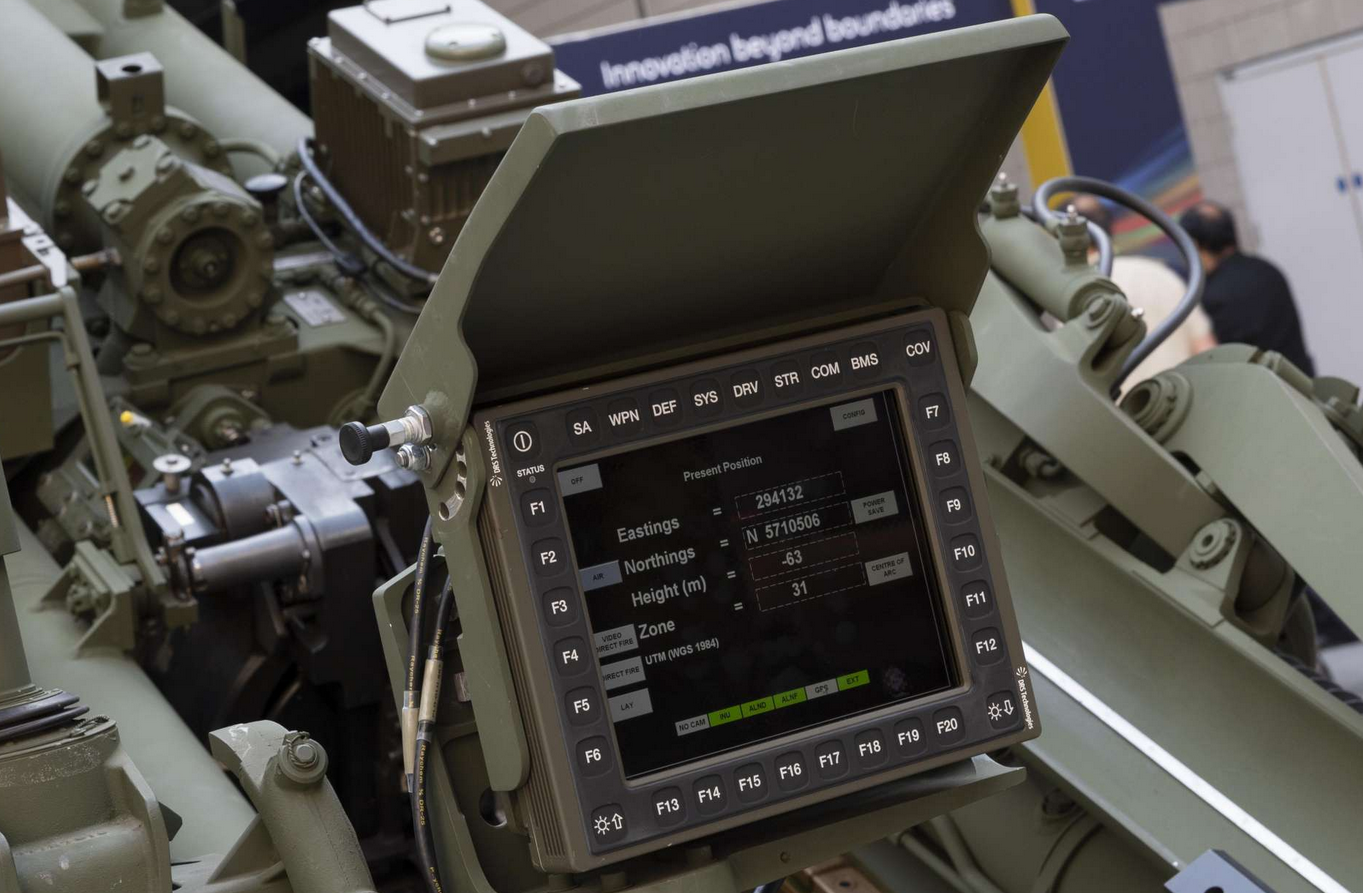 A Laser Inertial Artillery Pointing System (LINAPS) capability is seen with its screen displaying various details about its weapon's positioning (eastings, northings, height, zone, etc.). The screen has 32 buttons on its frame. Various mechanisms are seen on the back of the system. The whole unit is painted grayish green.
