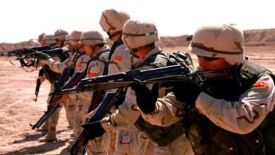 Seven soldiers from the Army of North Macedonia are seen pointing their rifles at something out of frame to the left. They are all wearing brown camo fatigues.