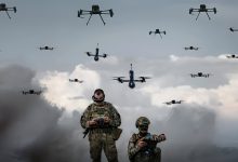 Two Ukrainian soldiers stand proudly in front of a lineup of military drones, showcasing their advanced technology.