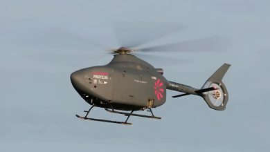 A small autonomous helicopter flying through the air against a clear blue sky.