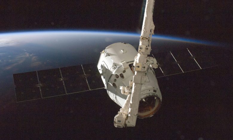 A SpaceX Dragon spacecraft orbits Earth with its solar arrays deployed.