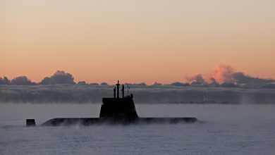 A military submarine emerges through dense sea mist under a dramatic orange dawn sky, used to illustrate Indra's development of a new satellite link to extend submarine connectivity at sea